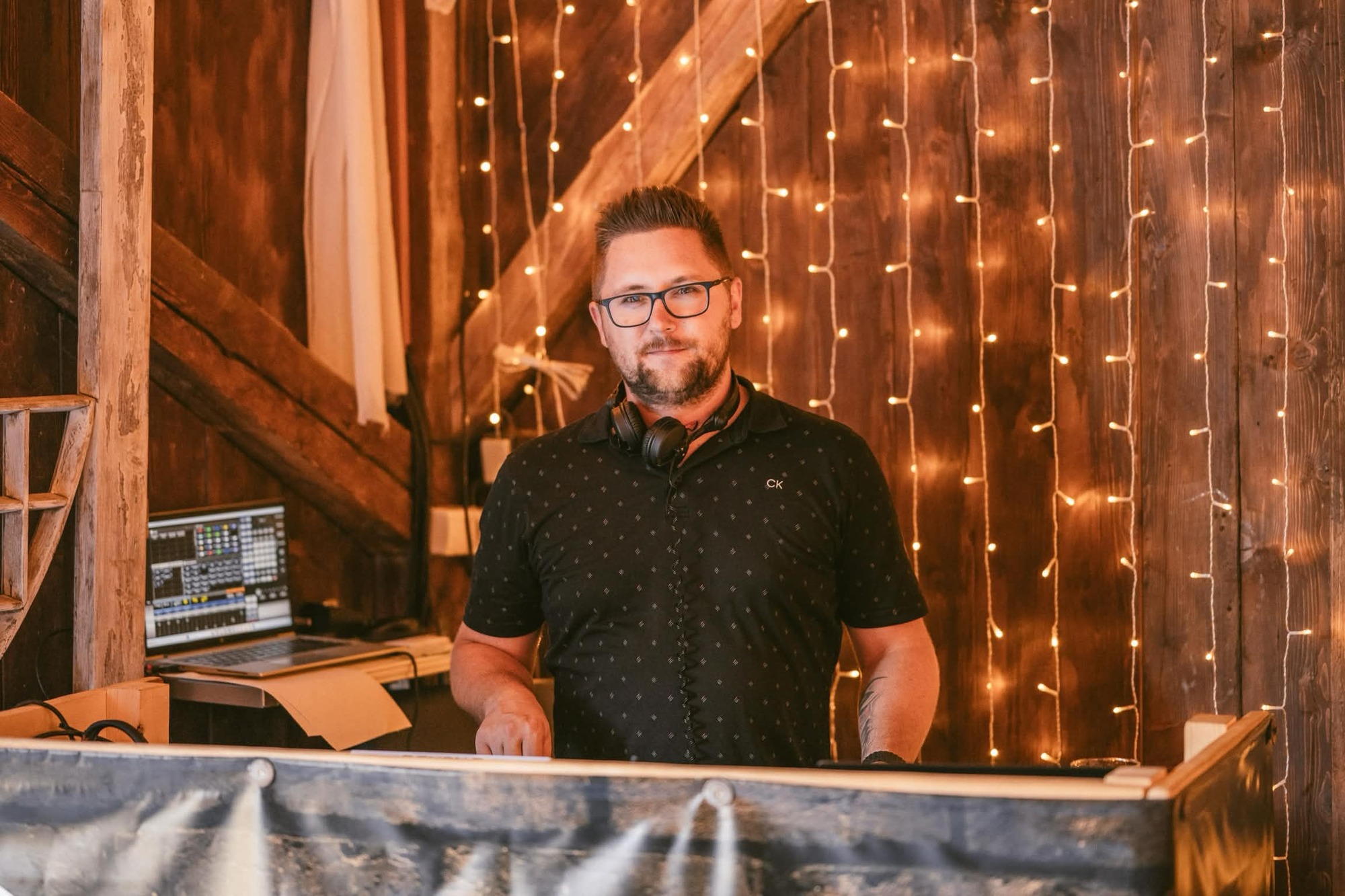 Václav Uličný za DJ pultem ve stodole s teplými světýlky
